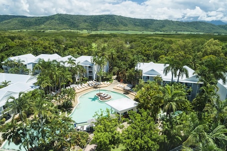 A resort with a central pool, multiple white-roofed buildings, and lush greenery.