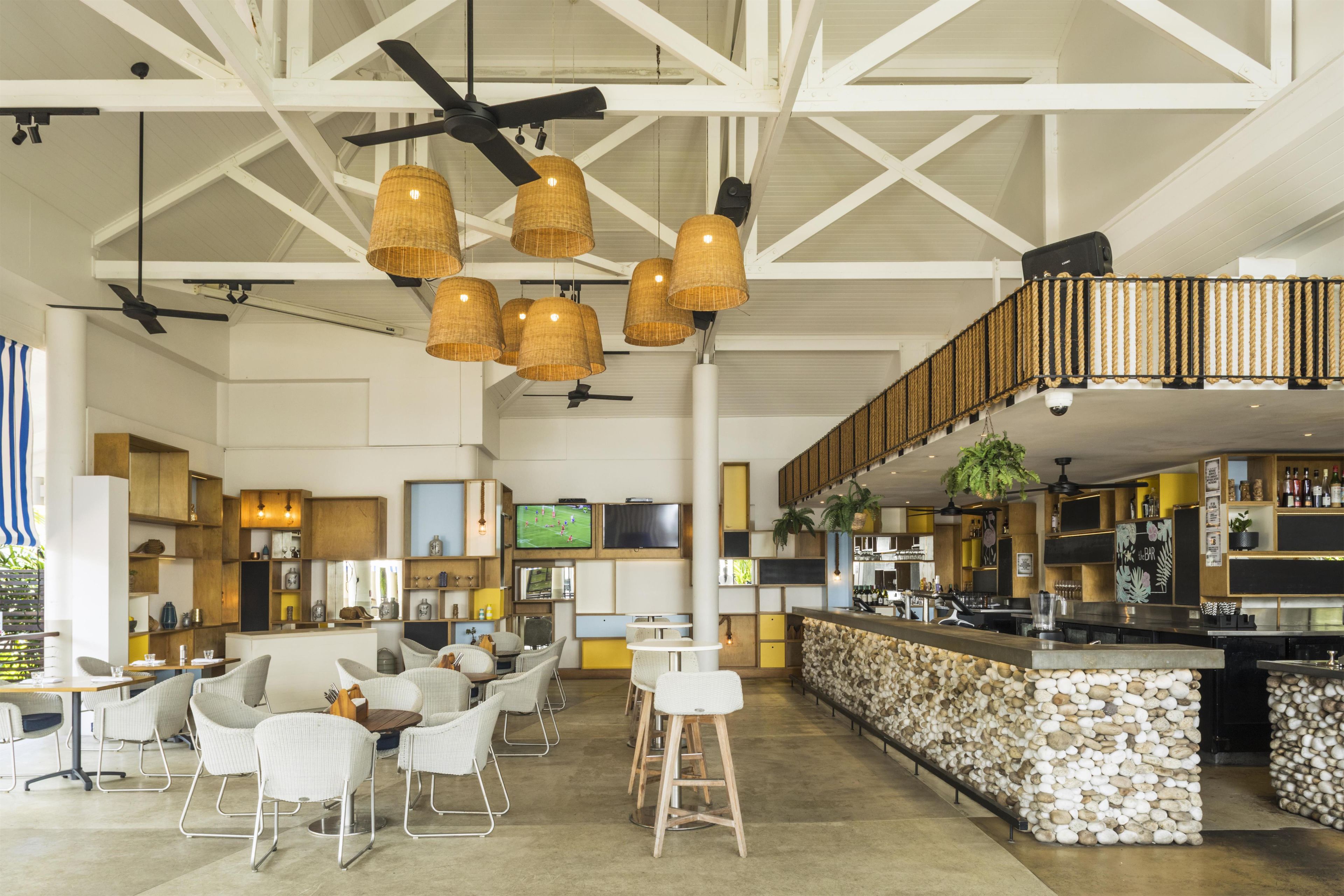 A spacious bar area with a stone counter, white bar stools, and a television mounted on the wall.