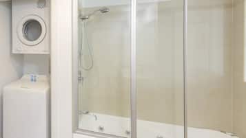 Un baño con ducha envuelta en vidrio, lavadora integrada y bañera.