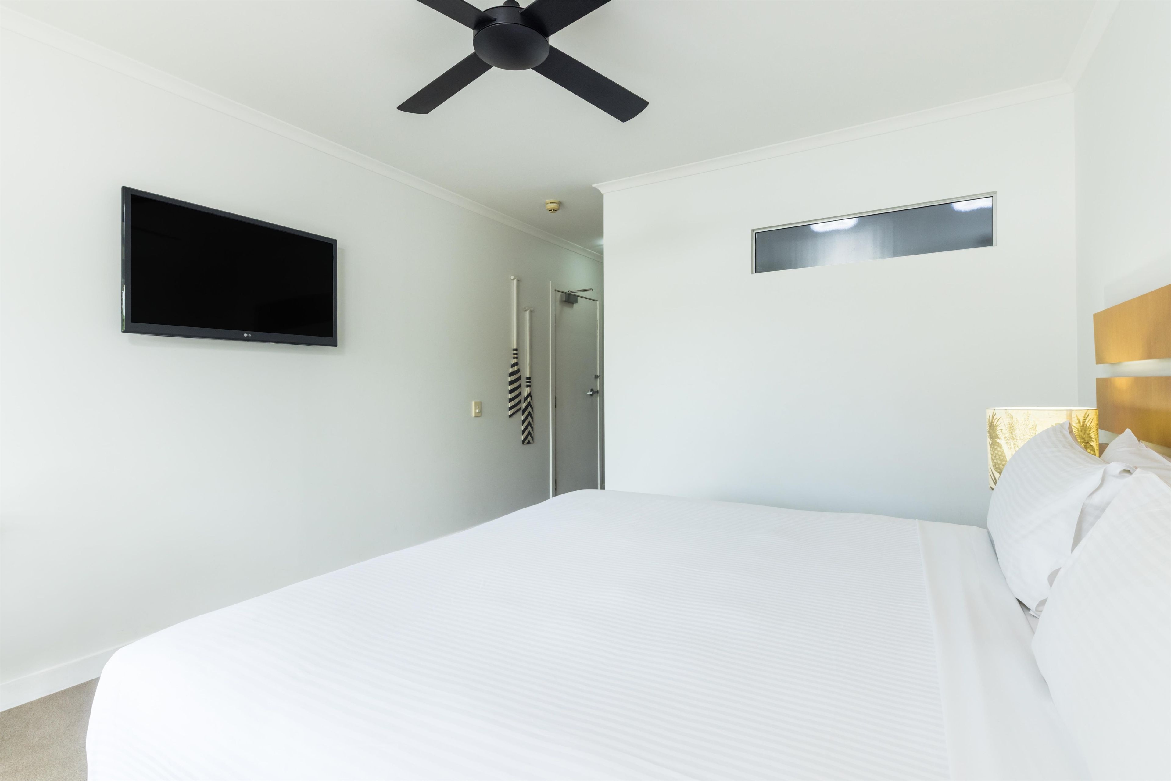 Une chambre d’hôtel équipée d’un lit, d’un ventilateur de plafond, d’un téléviseur à écran plat et d’une porte donnant accès à une salle de bain.