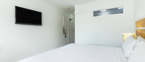 A hotel room with a bed, a ceiling fan, a flat-screen TV, and a door leading to a bathroom.