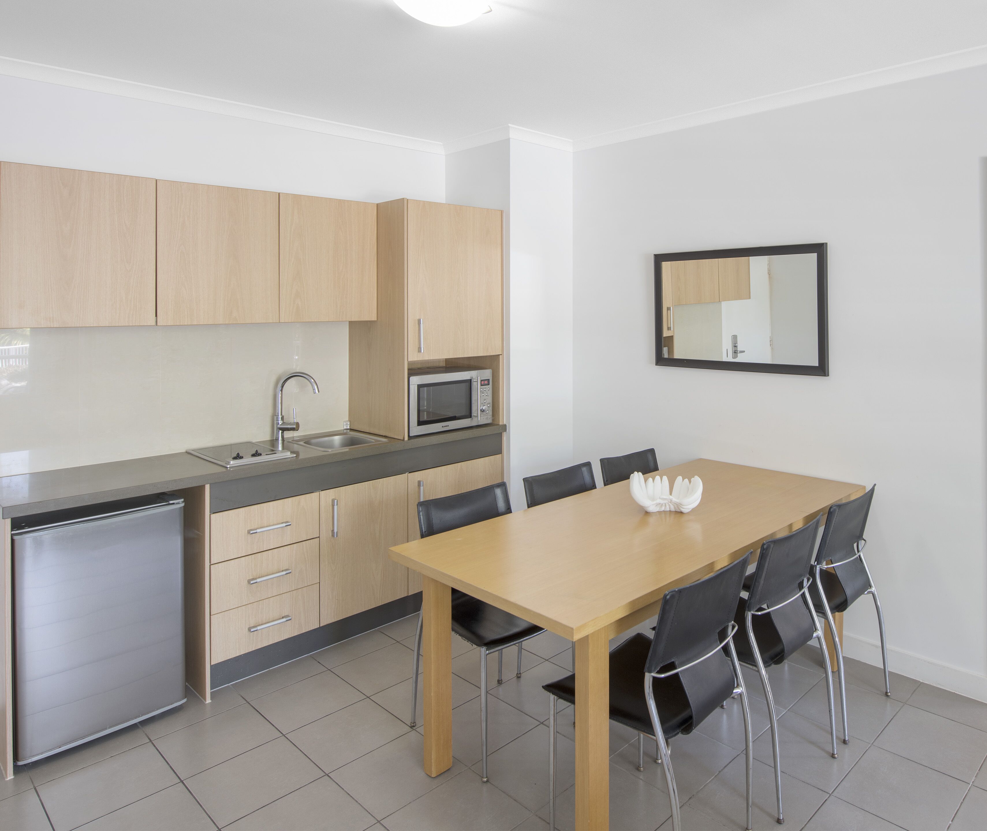 Una cocina moderna con armarios de madera, microondas, lavamanos y un comedor con mesa y sillas.