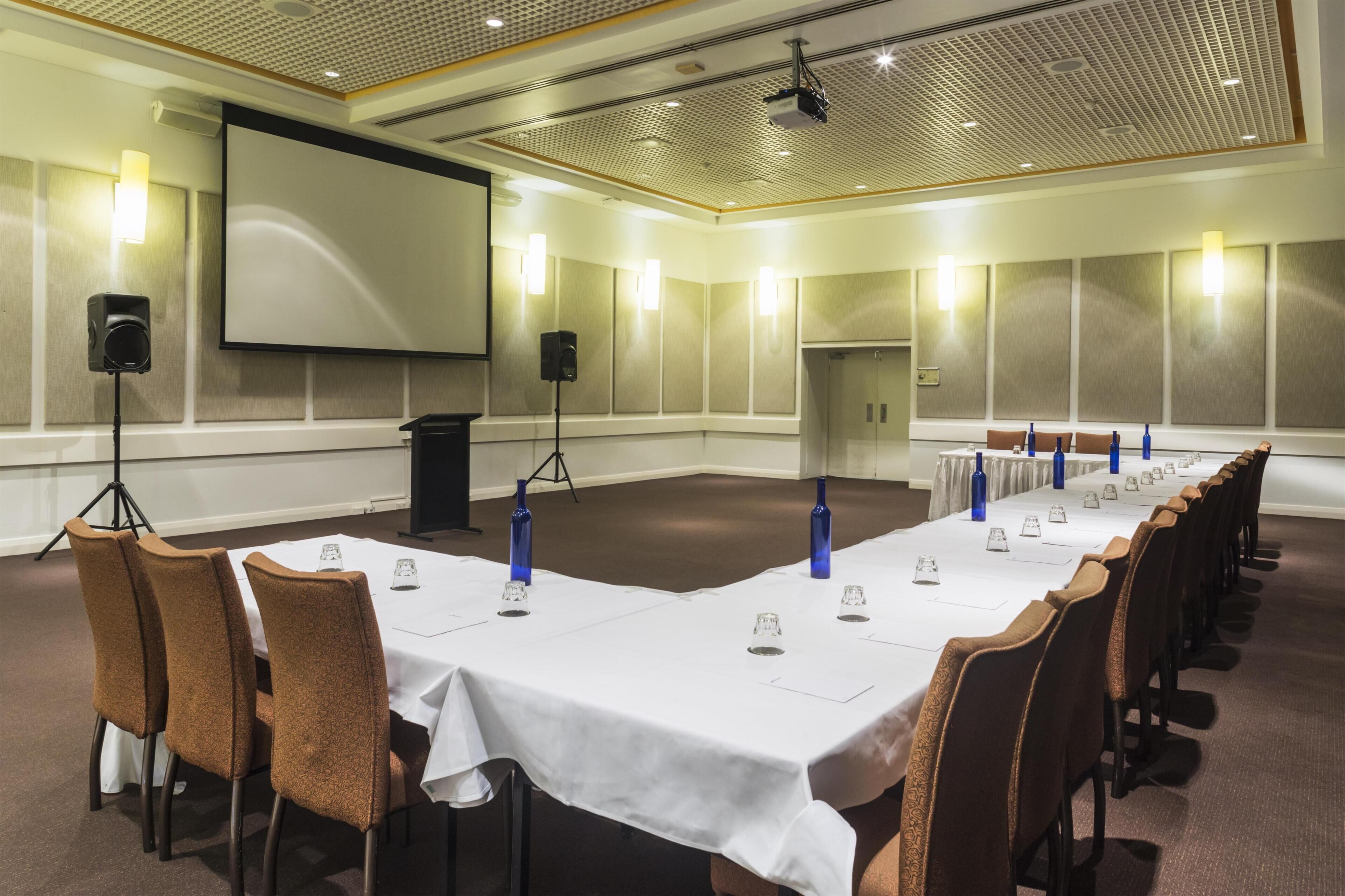 A conference room with a long table, chairs, a projector screen, and a whiteboard.