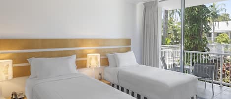 Et hotelværelse med to senge, en loftsvifte, en balkon med udsigt over grønne områder og et natbord med lampe og telefon.