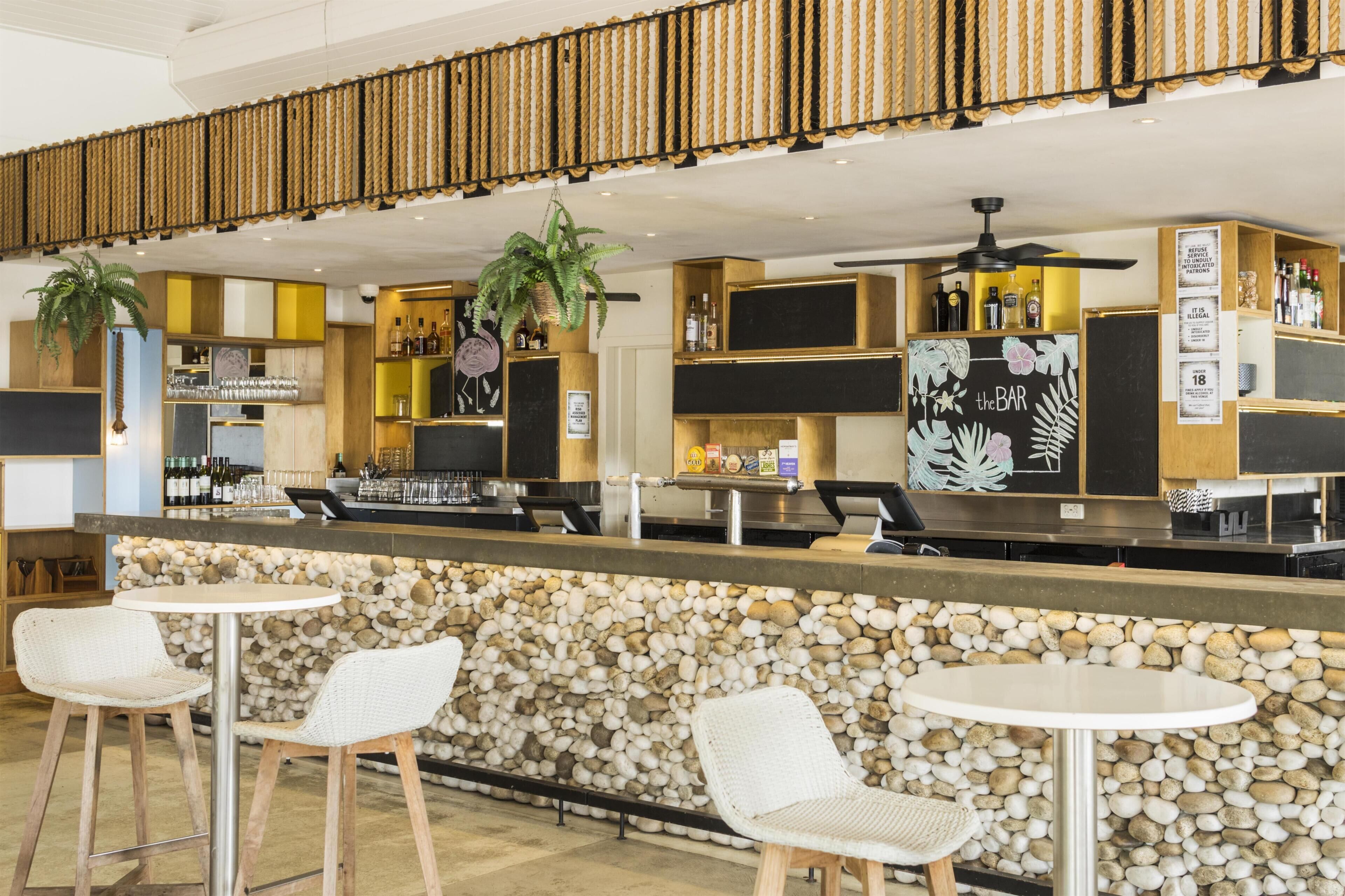 A bar area with a stone wall, white wicker chairs, and a counter with bottles and glasses.
