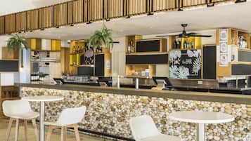 A bar area with a stone wall, white wicker chairs, and a counter with bottles and glasses.