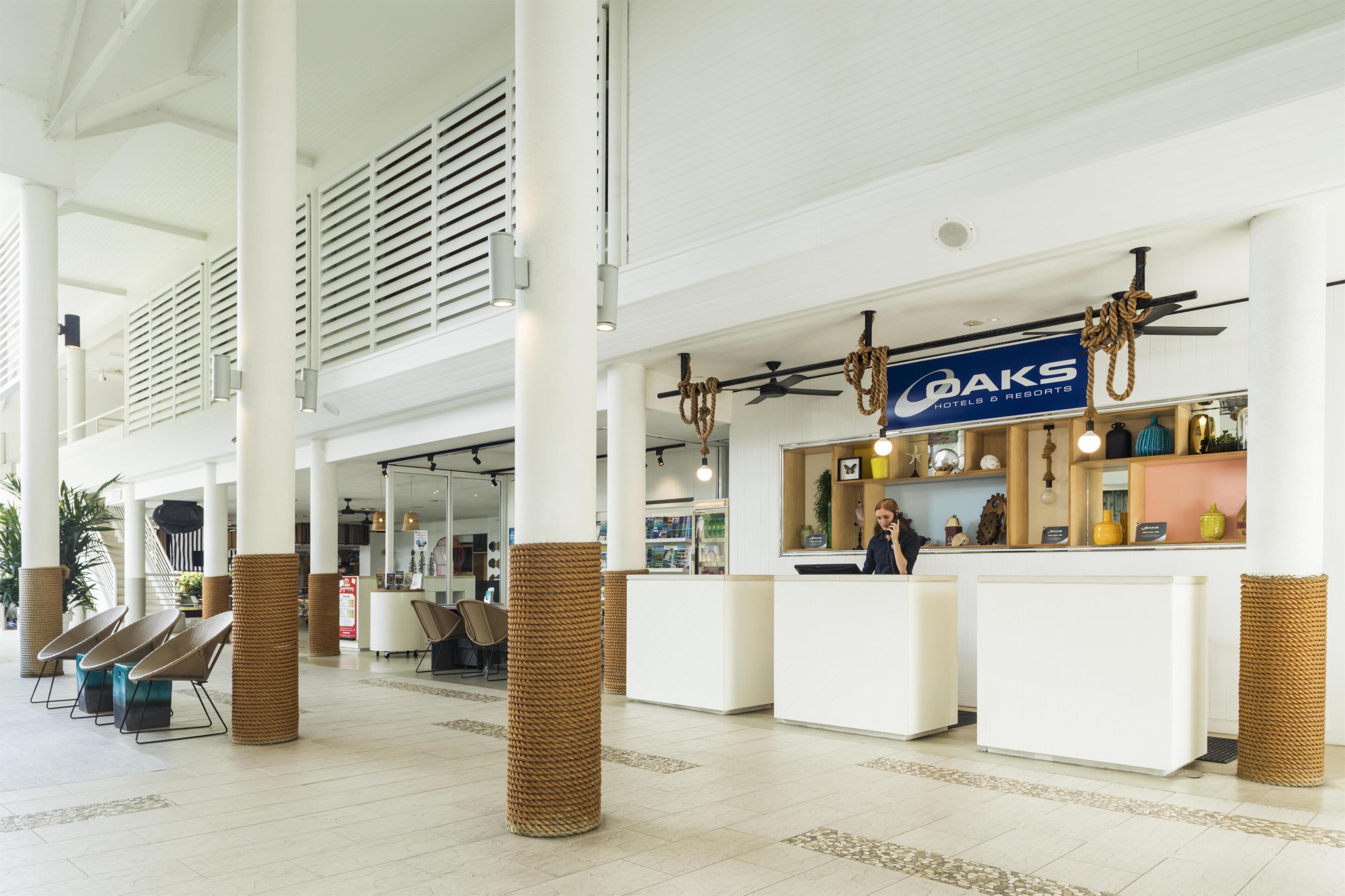 Un hall d’hôtel comprenant un comptoir d’accueil, un espace salon et un panneau indiquant « OAKS Hotels & Resorts ».