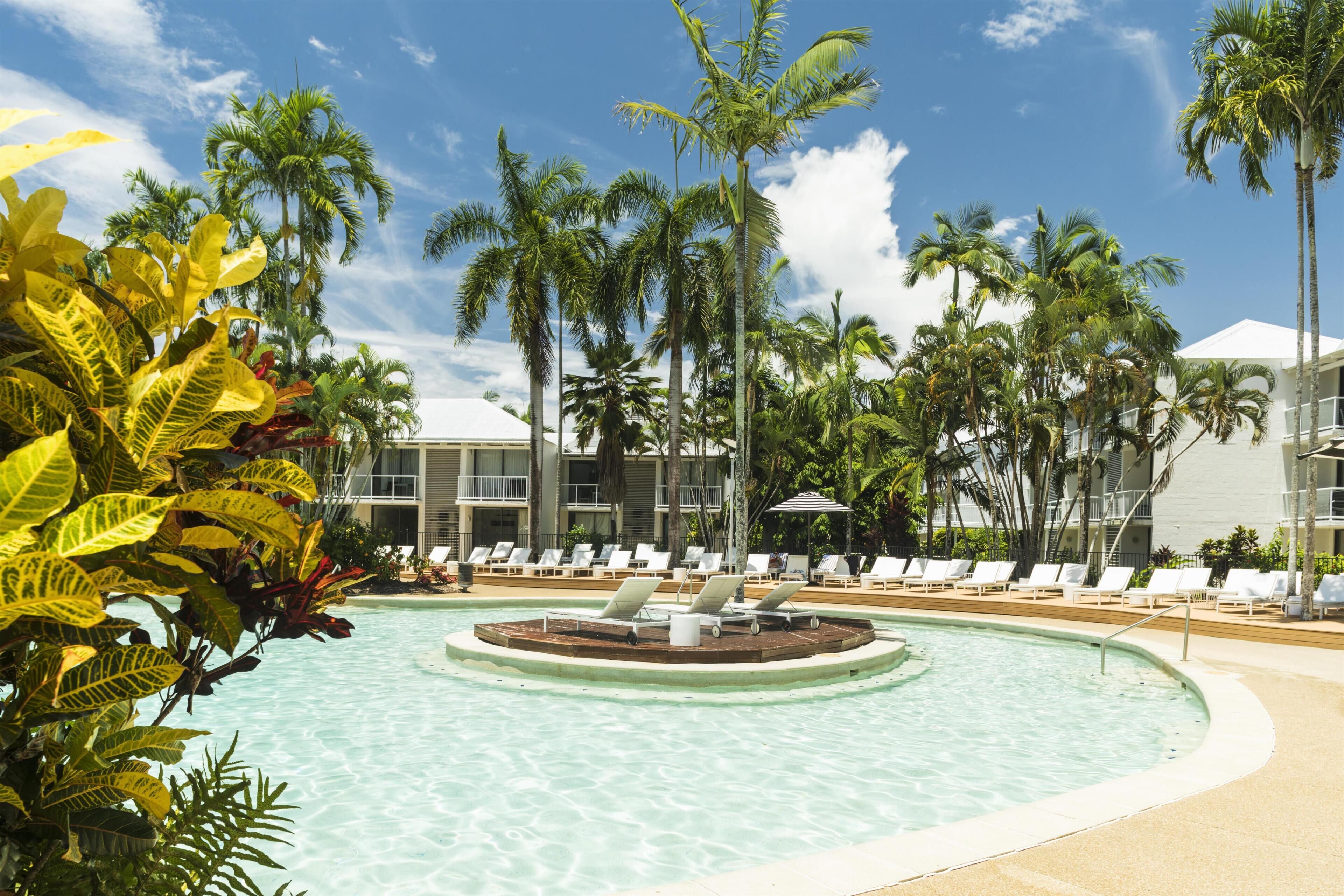 A pool with lounge chairs, palm trees, and a building with a white roof.