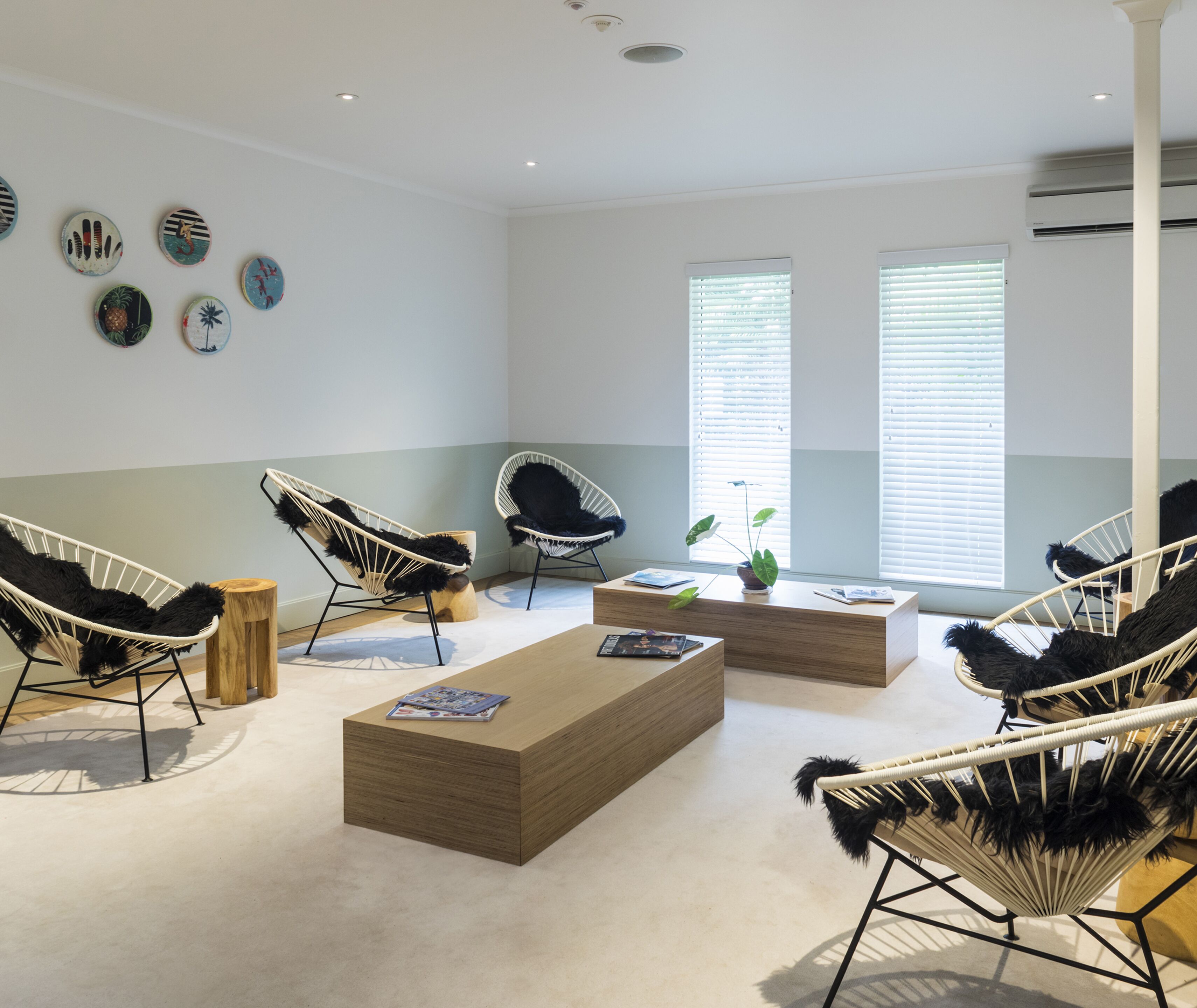 A modern, well-lit room with a wooden coffee table, two black and white wicker chairs, a wooden side table, and a wall decorated with circular art pieces.