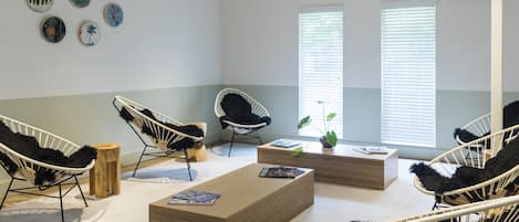 A modern, well-lit room with a wooden coffee table, two black and white wicker chairs, a wooden side table, and a wall decorated with circular art pieces.