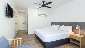 Una habitación de hotel moderna con cama, televisión, ventilador de techo, mesita de noche y suelo de madera.