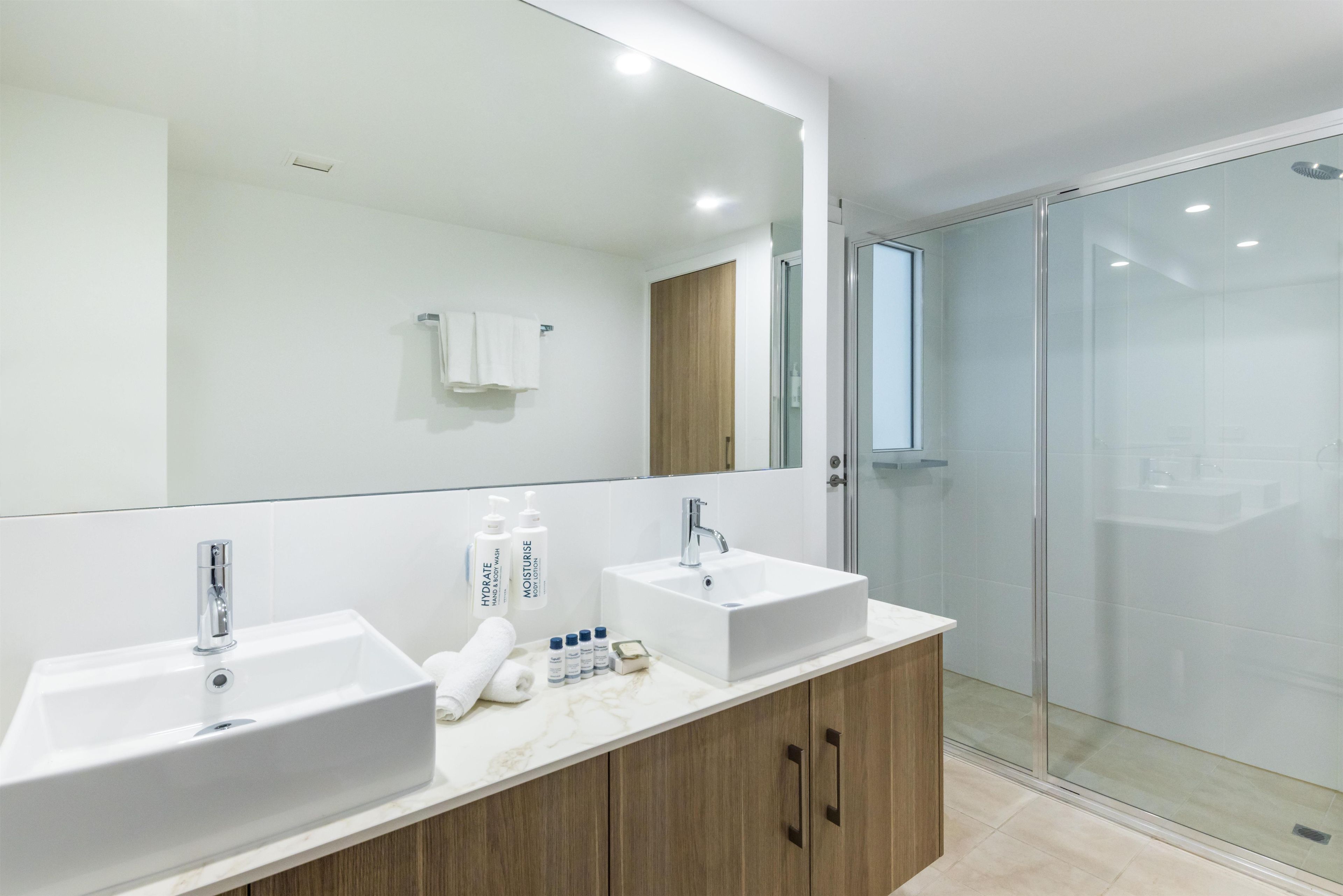 A modern bathroom with two sinks, a large mirror, and a glass shower enclosure.