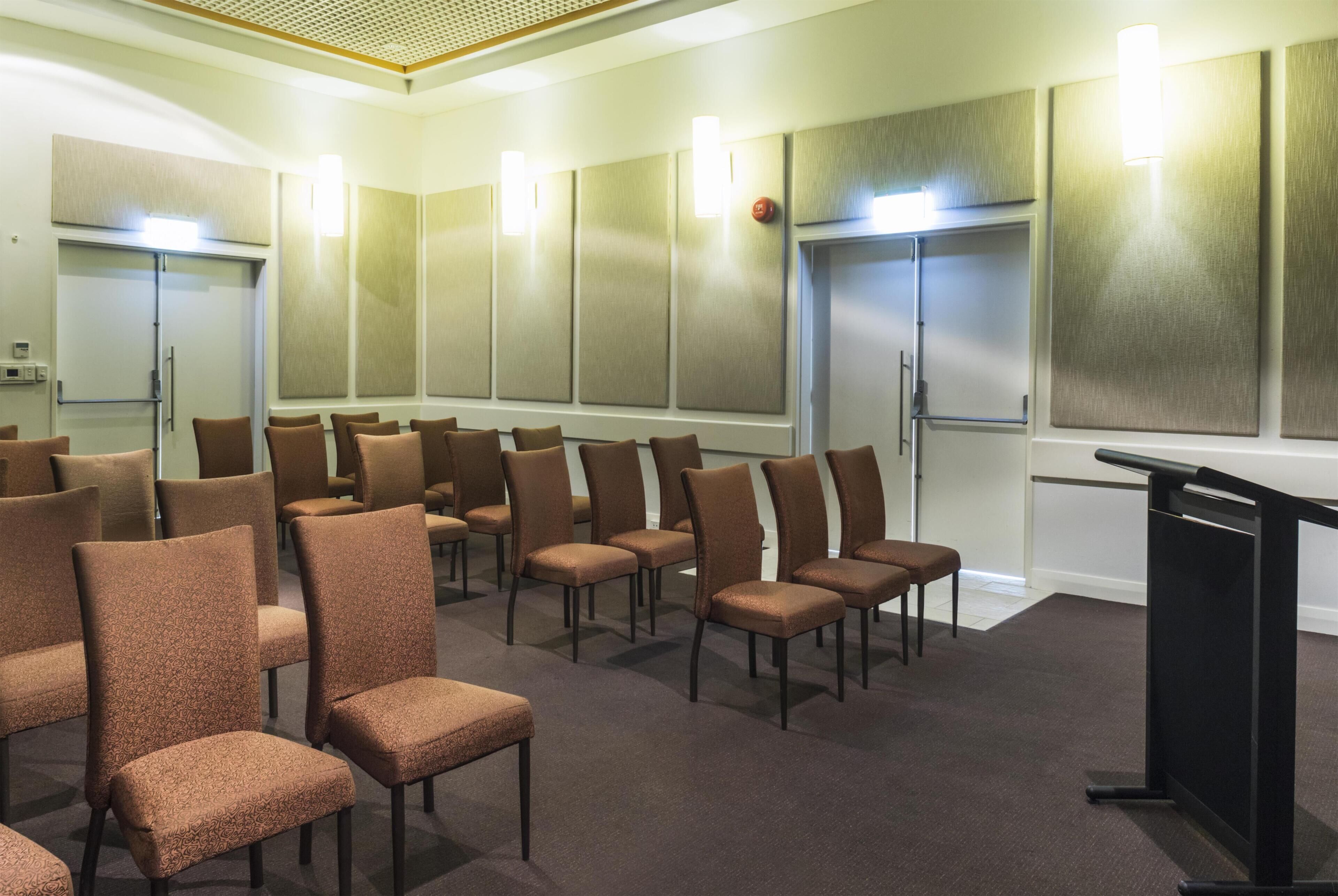 Une salle de conférence avec des rangées de chaises, un pupitre et des panneaux d’insonorisation sur les murs.