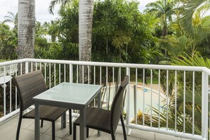 A balcony with a glass table and wicker chairs, surrounded by palm trees and a pool. - Oaks Port Douglas Resort (Port Douglas)