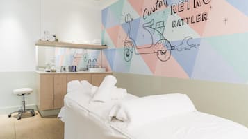 Et hotelværelse med en seng, et skrivebord med stol, et spejl og en væg med et farverigt geometrisk mønster.