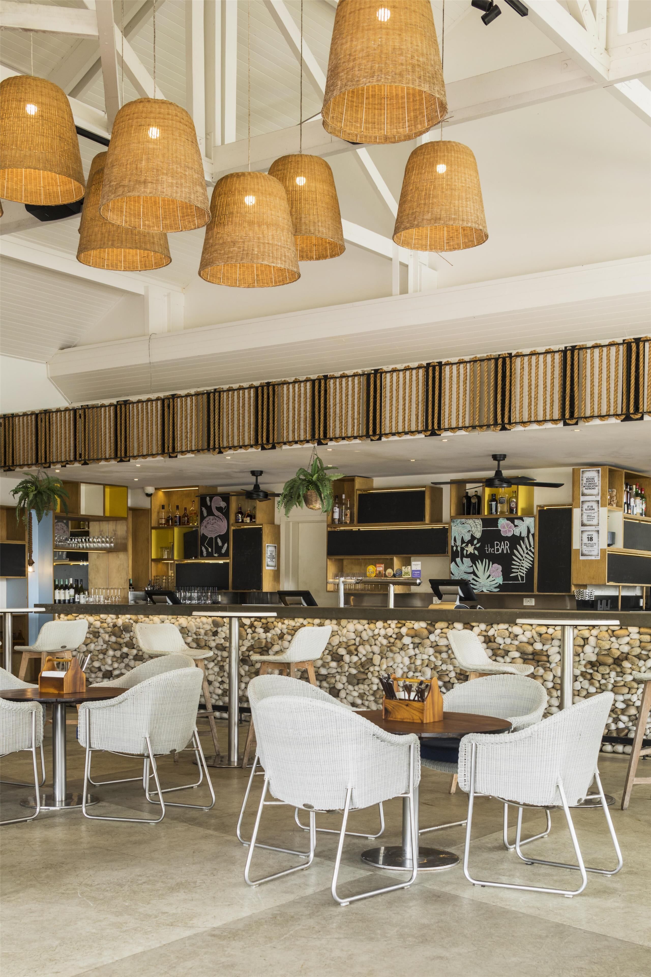 A modern bar area with wicker pendant lighting, white wicker chairs, and a stone wall backdrop.