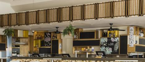 A modern bar area with wicker pendant lighting, white wicker chairs, and a stone wall backdrop.