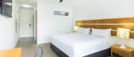 Habitación de hotel con cama, mesita de noche, silla, ventilador de techo, televisor y una puerta que da a otra habitación.