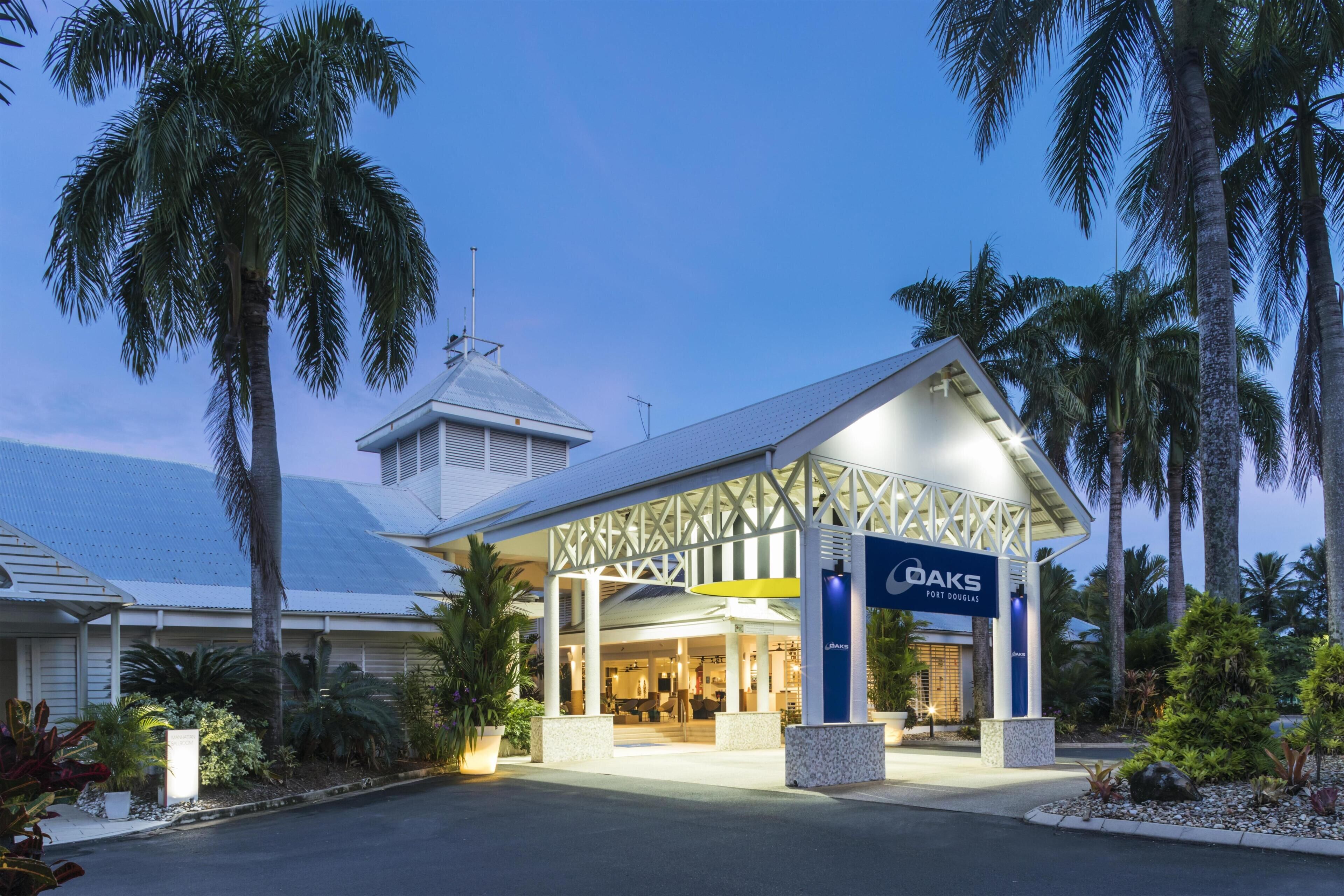 A hotel with a covered entrance, palm trees, and a sign reading 'OAKS Fort Douglas.'