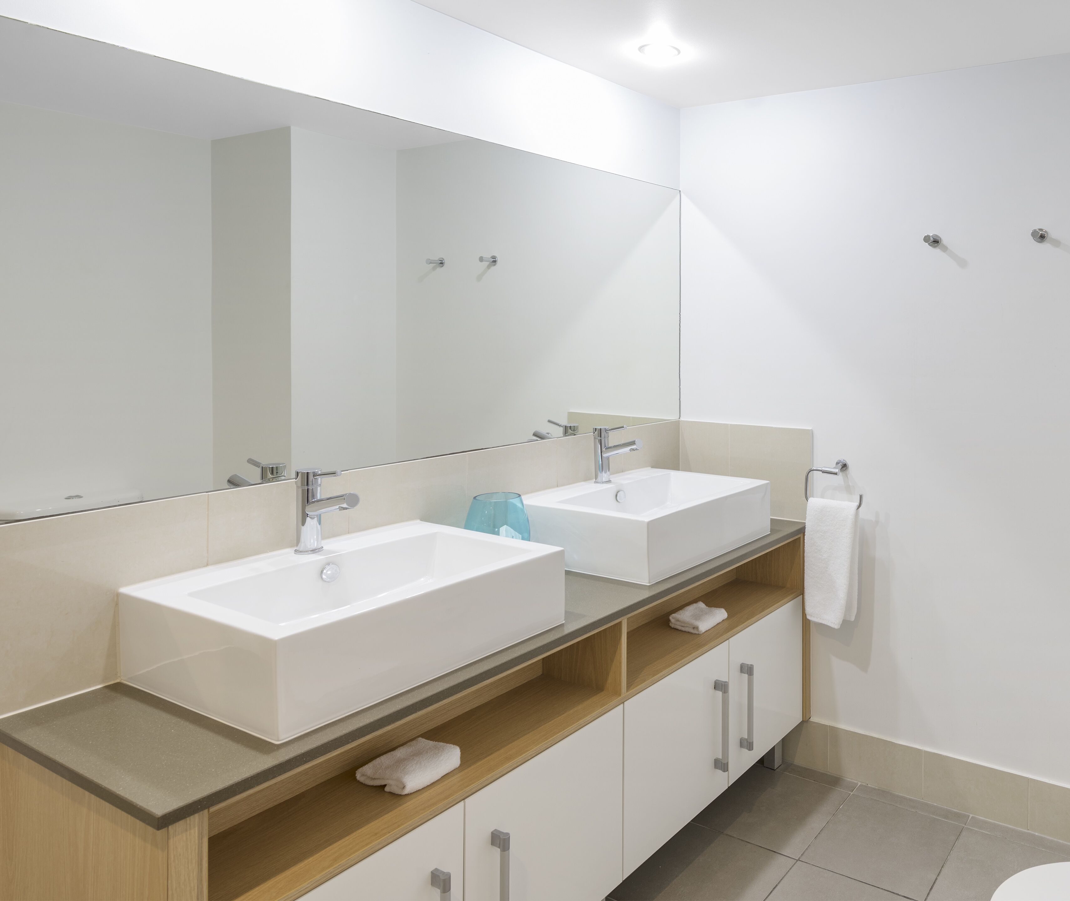 A modern bathroom with two sinks, a large mirror, and a wooden vanity.