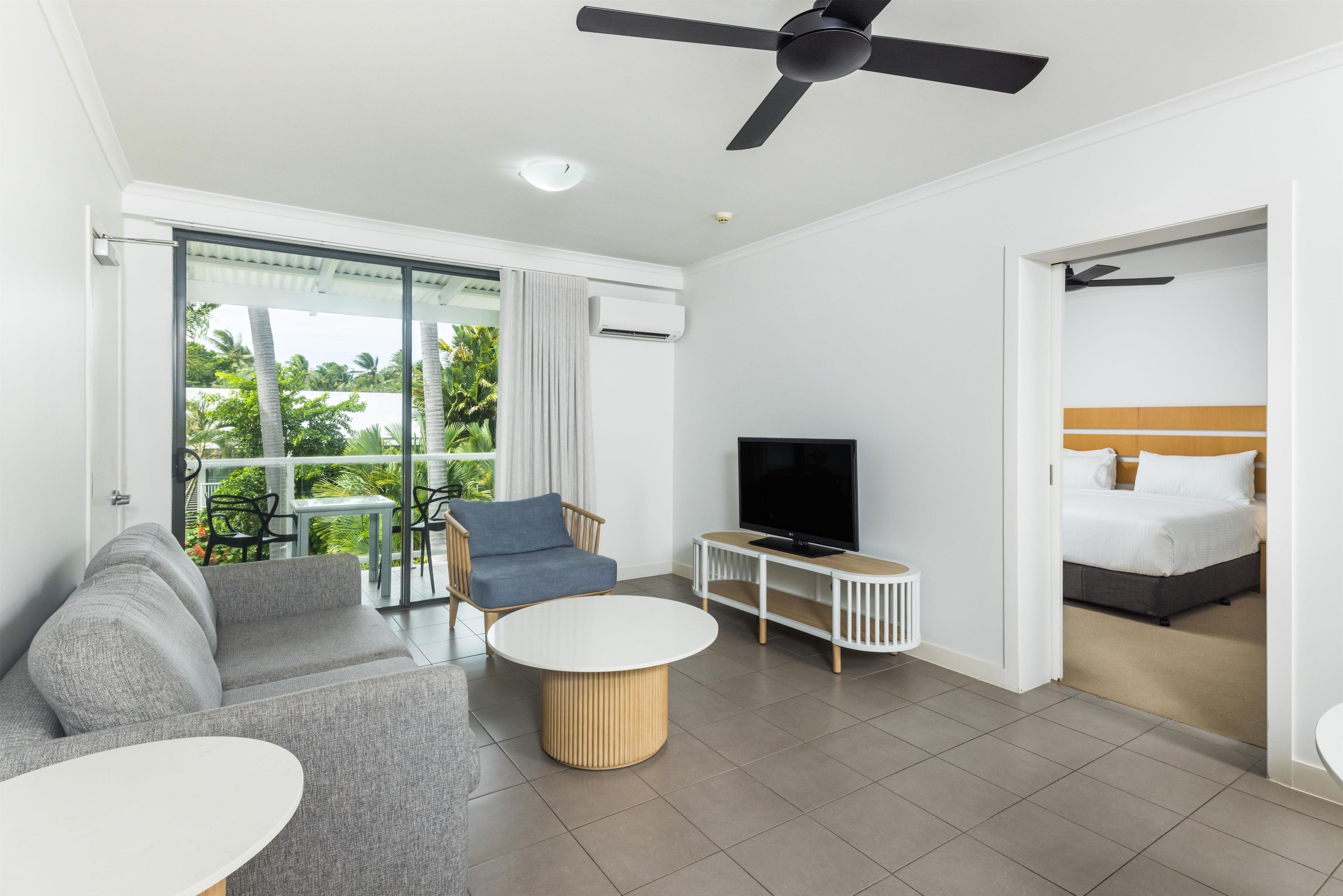 A modern hotel room with a sofa, TV, and a balcony with a view of greenery.