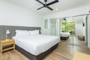 Ein modernes Schlafzimmer mit einem großen Bett, einem Deckenventilator, einem Nachttisch, einer Schiebetür zu einem Außenbereich und Holzboden.