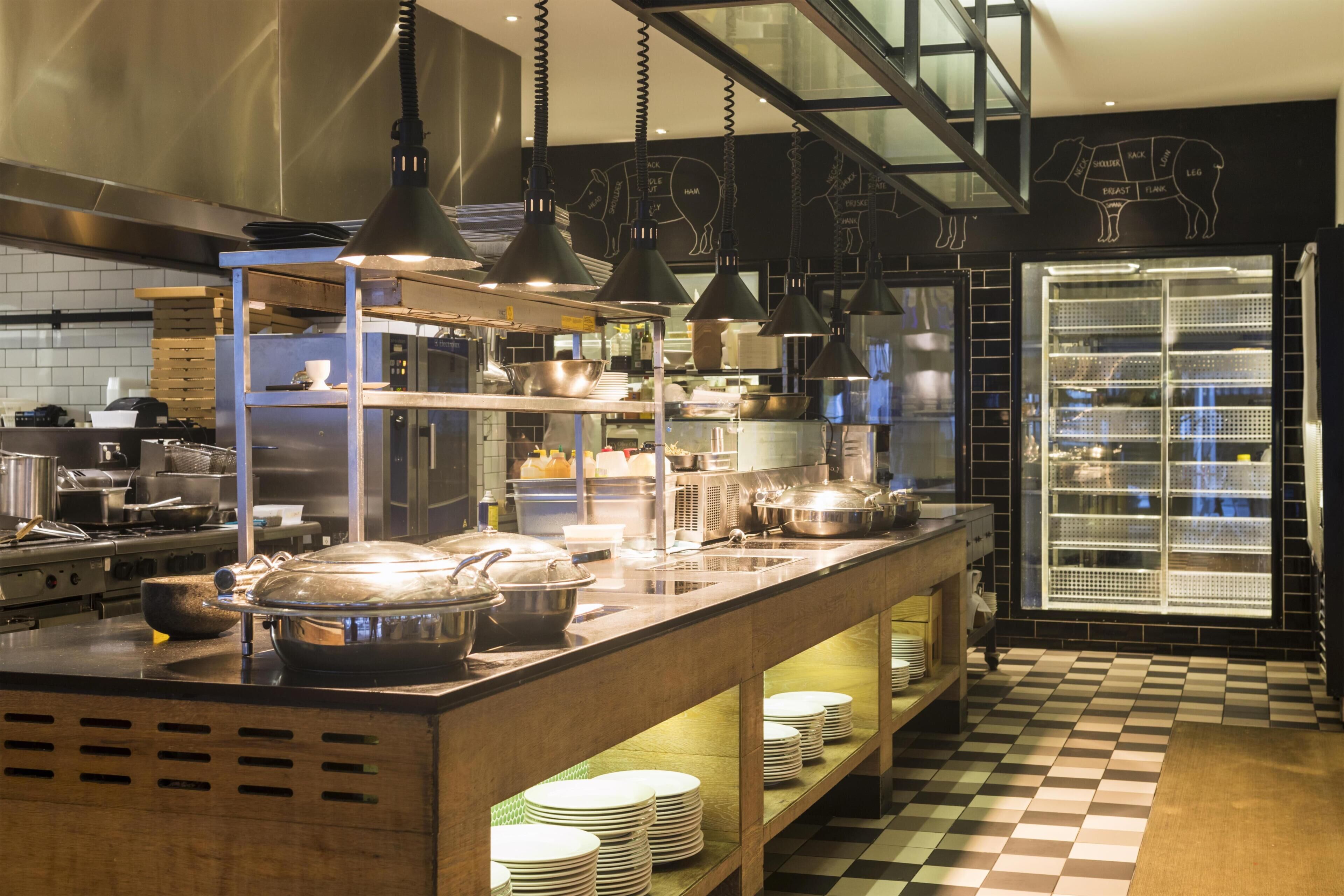 Une cuisine moderne dotée d’appareils électroménagers en acier inoxydable, de luminaires suspendus et d’un sol à carreaux.