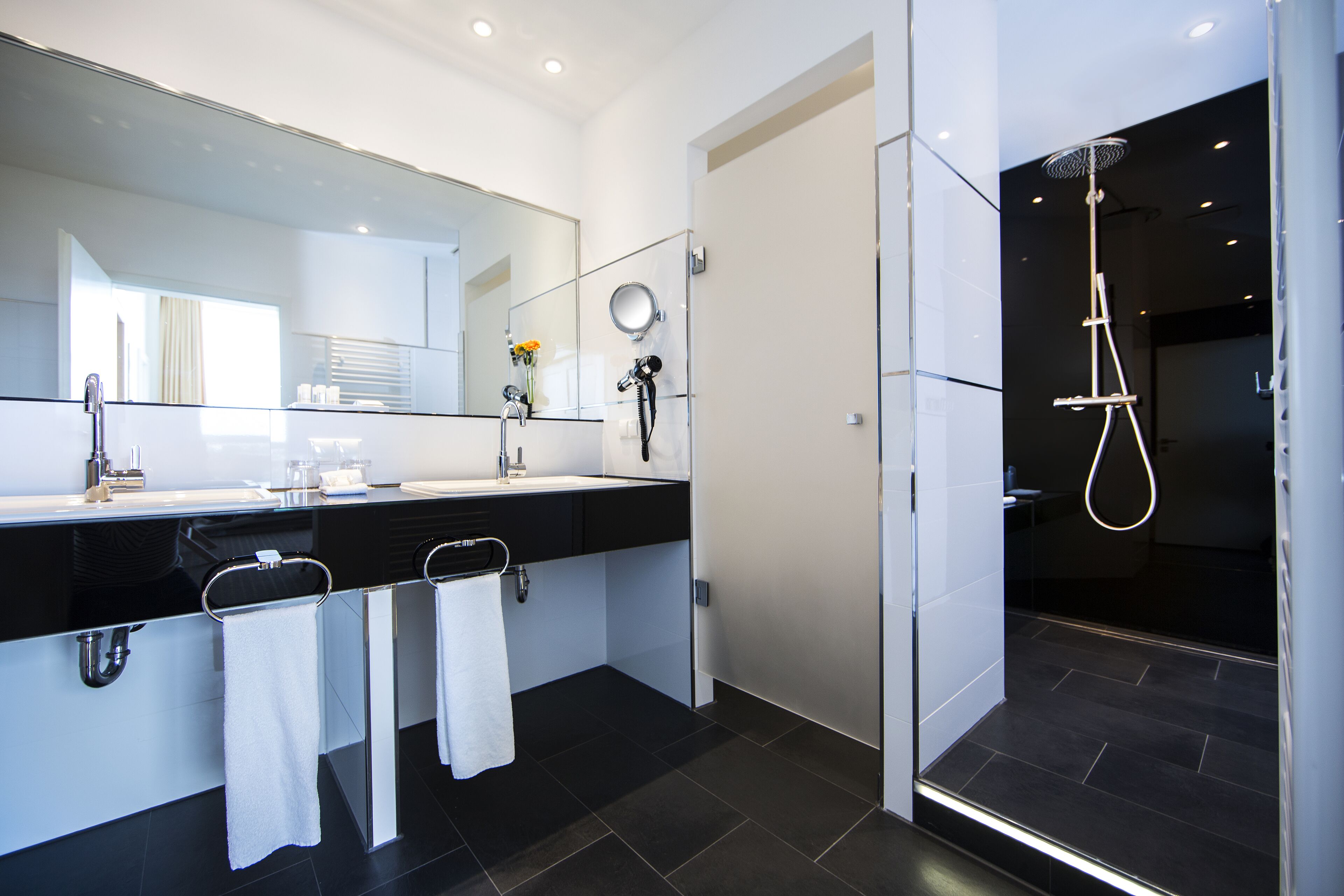 A modern bathroom with a large mirror, two sinks, a shower, and a glass-enclosed walk-in shower.