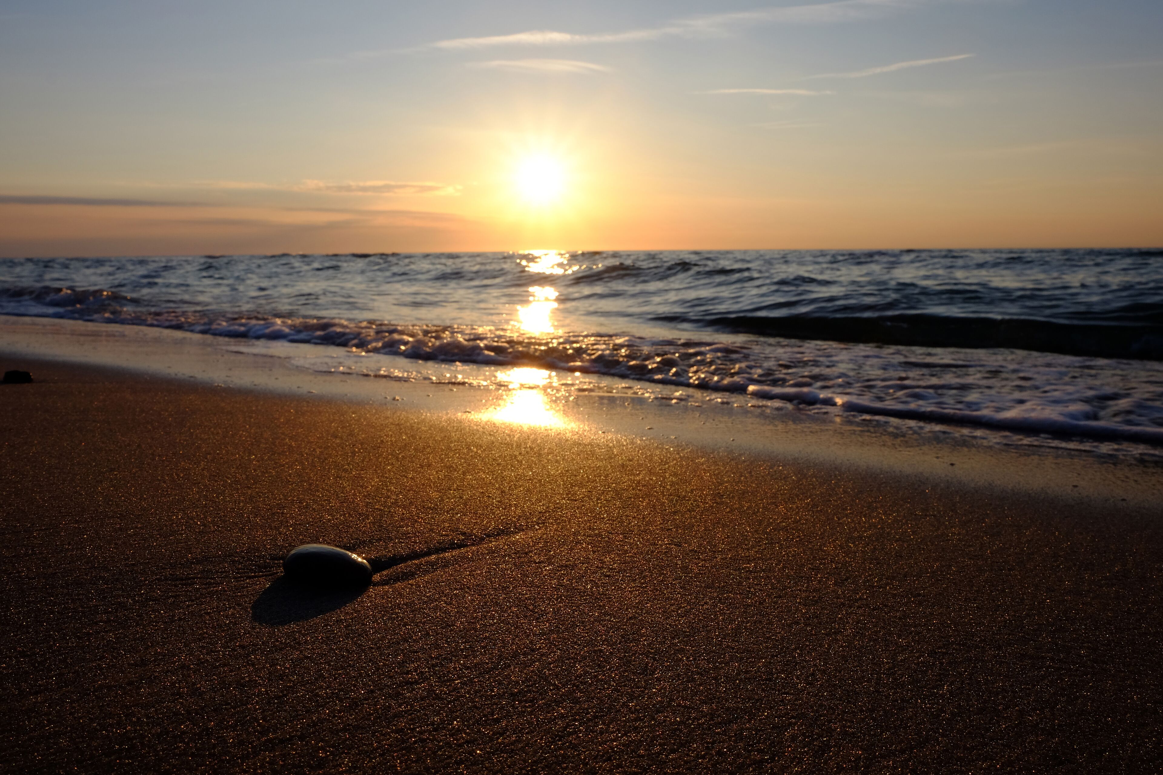 Uma praia ao pôr do sol, com areia fina e um único objeto na areia.
