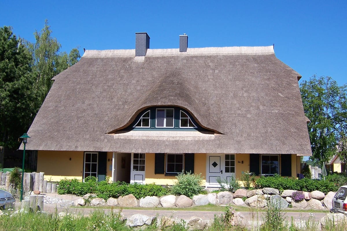 Ein Haus mit einem markanten, gewölbten Dach, einer Veranda mit einer Bank und einer Mauer aus großen Steinen.