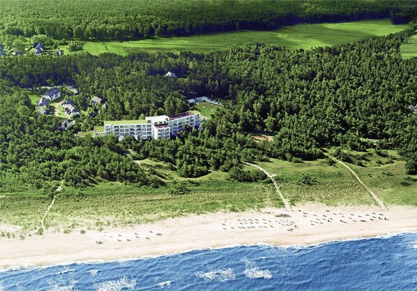 Vue aérienne d’une station balnéaire, avec un bâtiment central entouré d’une forêt dense, d’une plage de sable et d’un parcours de golf.