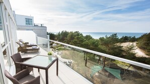 Ein Balkon mit Korbmöbeln, einem Glastisch und Blick auf Strand und Bäume.