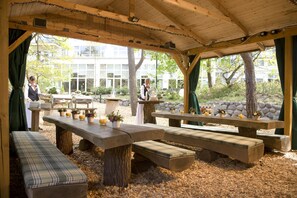 Un pavillon extérieur en bois, doté de tables et de bancs pour pique-nique, entouré d’arbres et d’un mur de pierre.