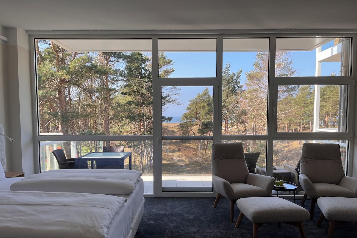 Ein Schlafzimmer mit großem Fenster, einem Bett und zwei Sesseln.