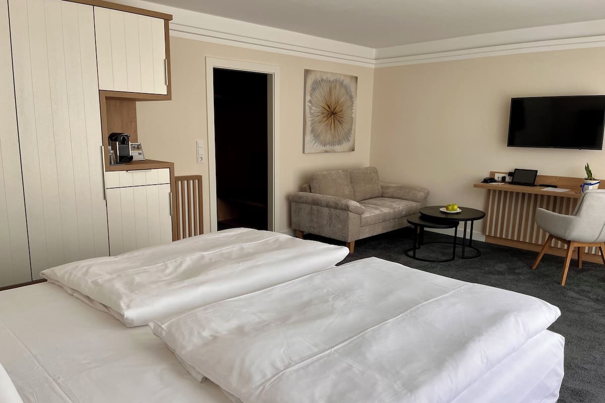 Ein Hotelzimmer mit zwei Betten, einem Schlafsofa, einem kleinen Tisch, einem Fernseher und einer Küchenzeile.