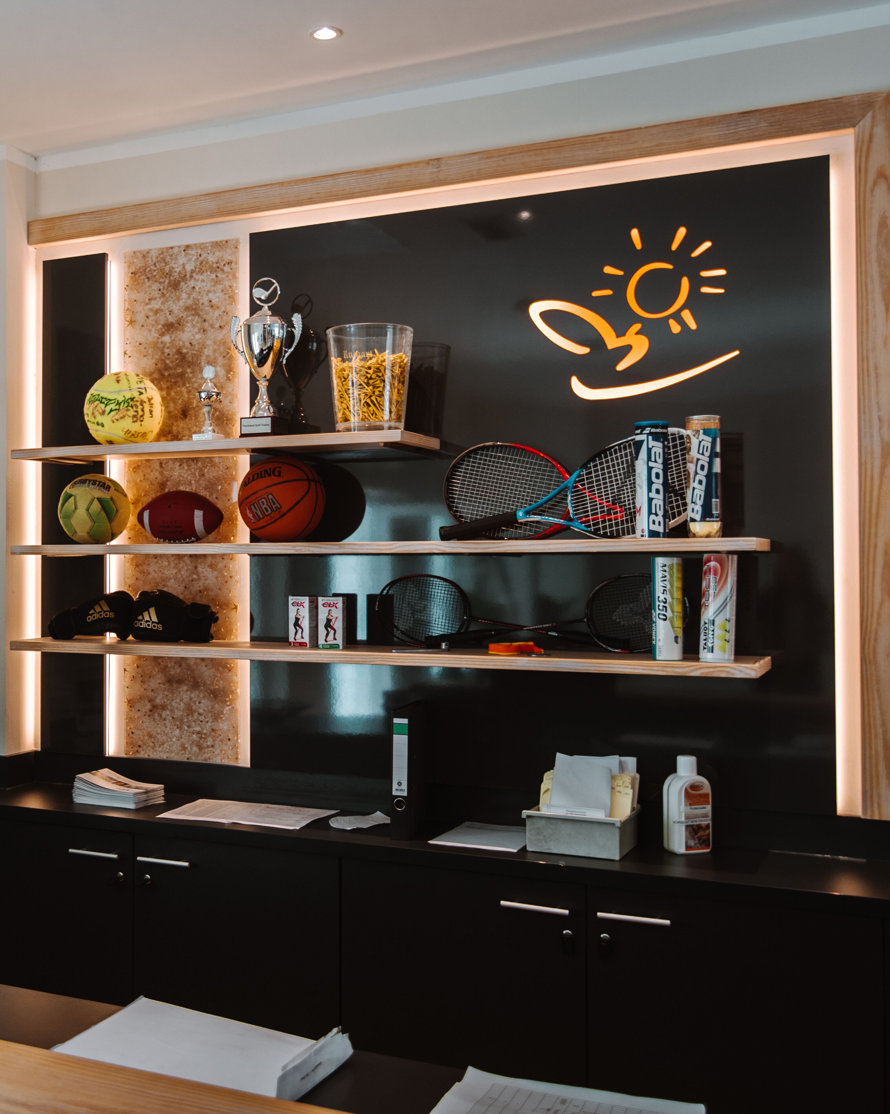 A sports-themed wall with shelves displaying trophies, sports balls, and rackets.