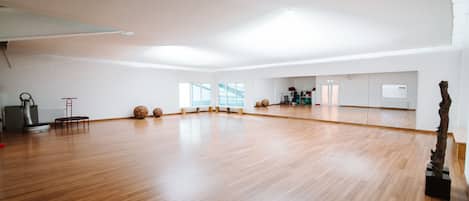 Una habitación amplia con suelo de madera, ventanas grandes y un espejo.