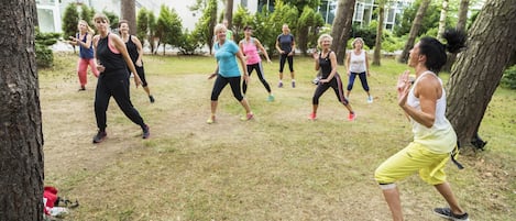A group of people exercising outdoors in a grassy area with trees and a building in the background.