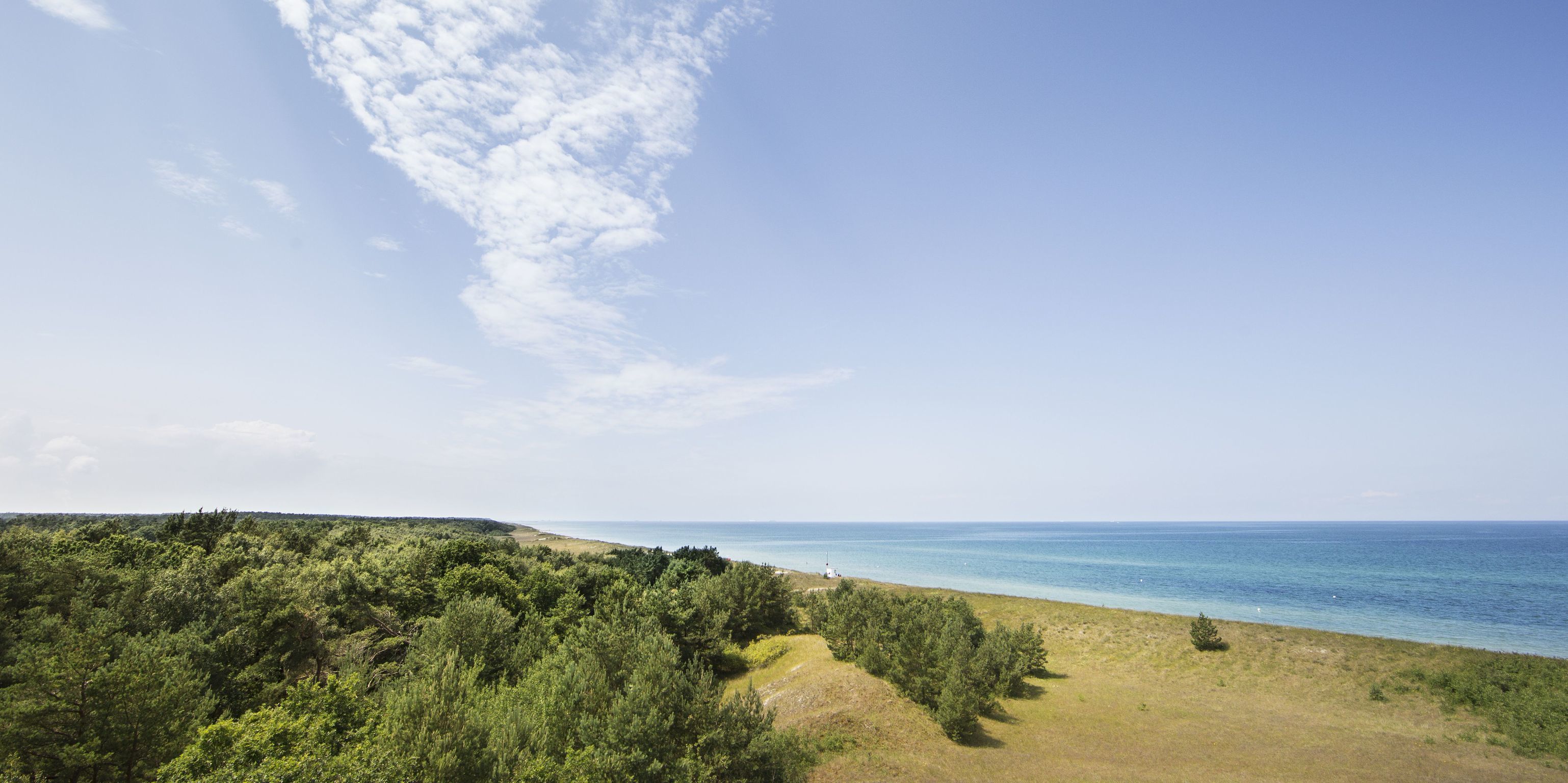 A coastal landscape with dense greenery and a clear view of the sea.