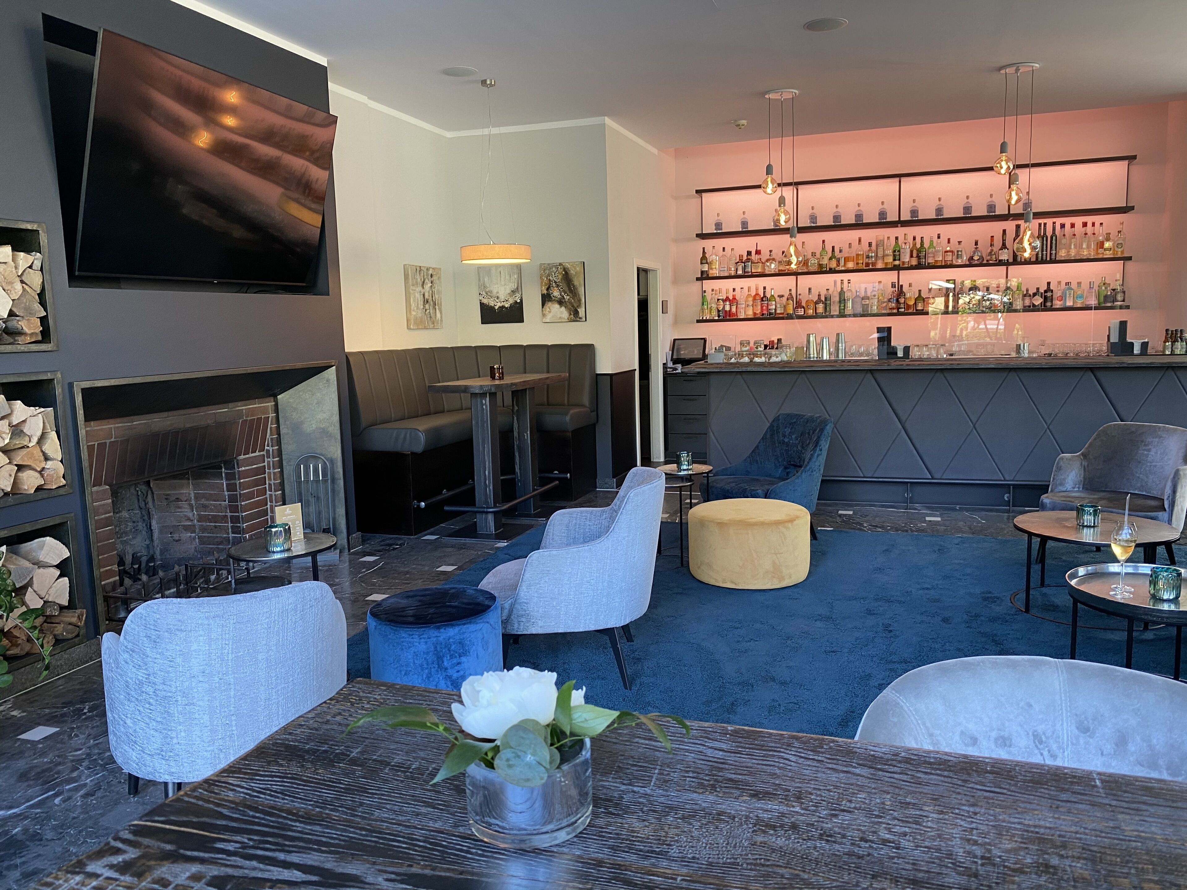 A modern lounge area with seating, a fireplace, a bar with shelves of bottles, and artwork on the walls.