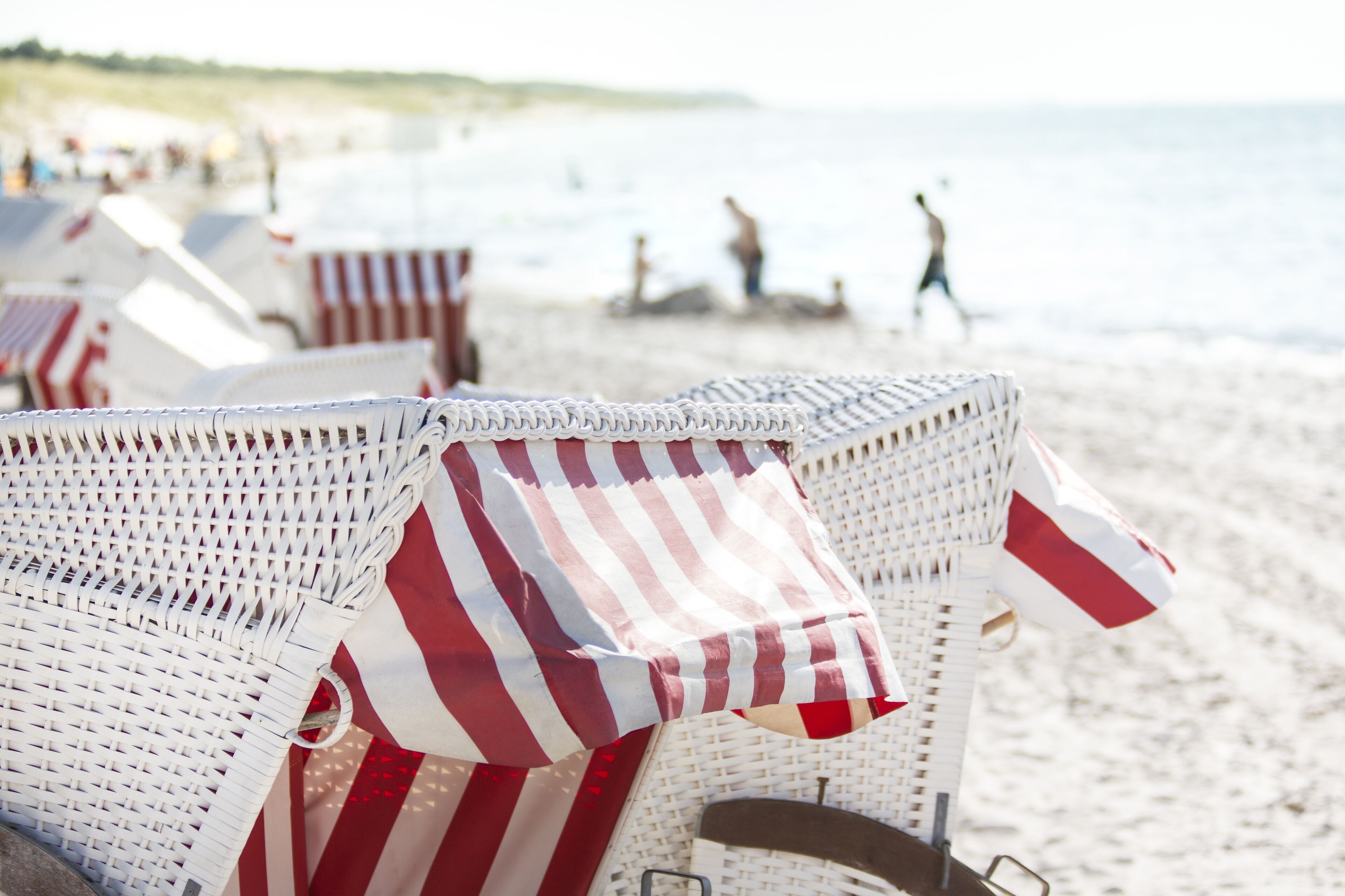 Wicker beach chairs with striped covers, a sandy beach, and people in the background.