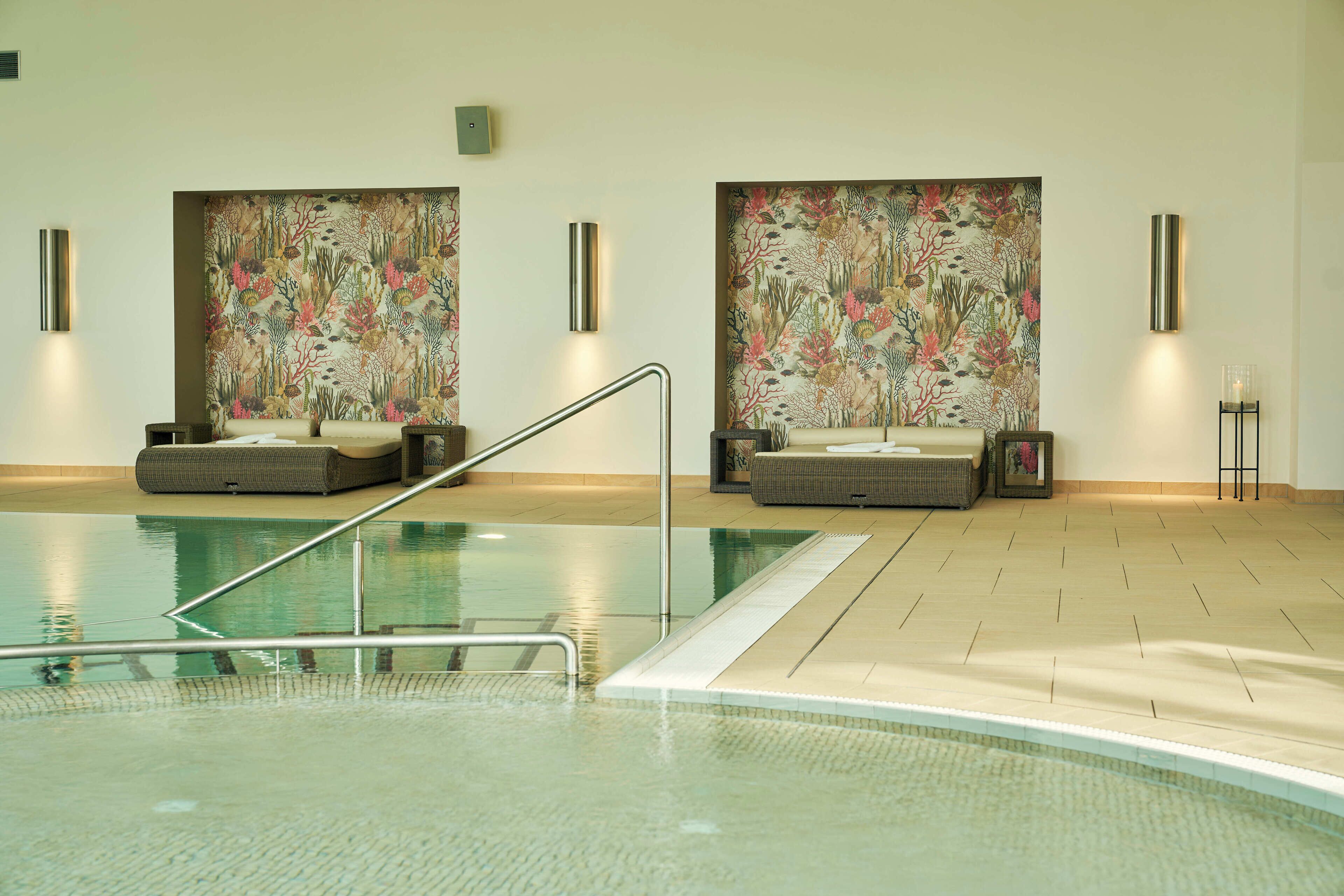 A swimming pool with two lounge chairs and a wall with floral artwork.