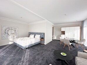 Une chambre d’hôtel moderne avec un grand lit, un coin repas avec des chaises et une petite table avec des pommes.