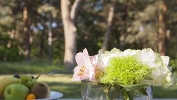 A glass vase with flowers and fruits on a table outdoors.