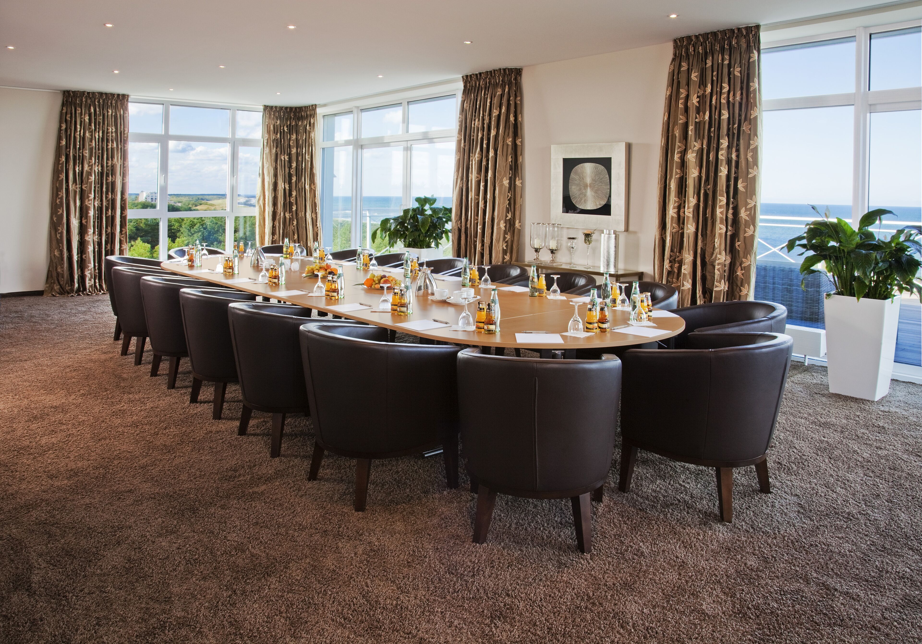 A conference room with a long table, black chairs, and a view of the sea.