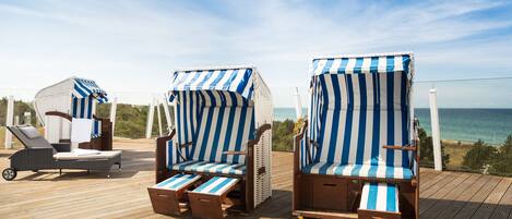 Dos sillas de playa con cojines azul y blanco a rayas sobre una terraza de madera con vista al mar.