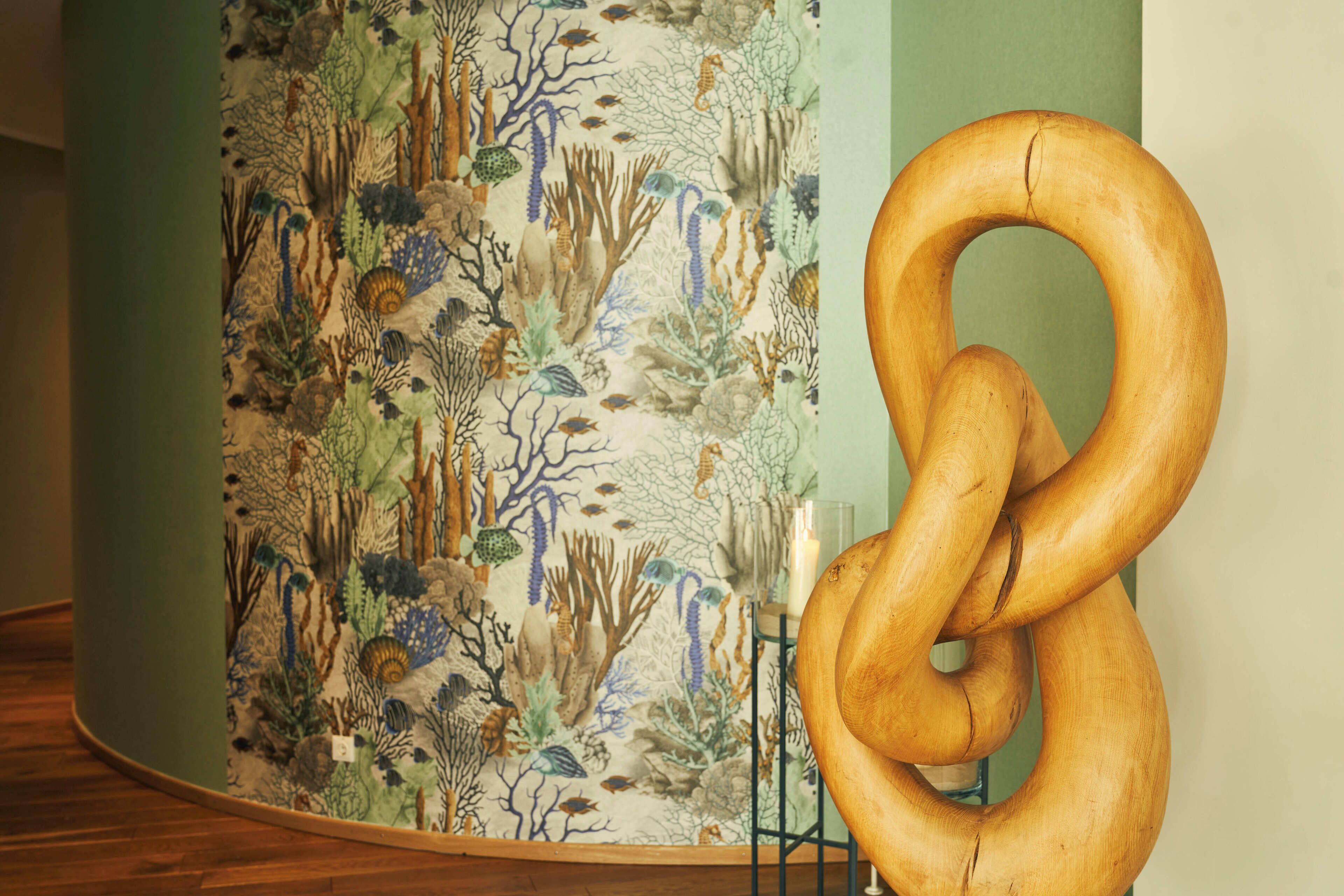 Une grande sculpture en forme de bretzel dans une pièce dont un mur est décoré d’une fresque représentant un paysage sous-marin.