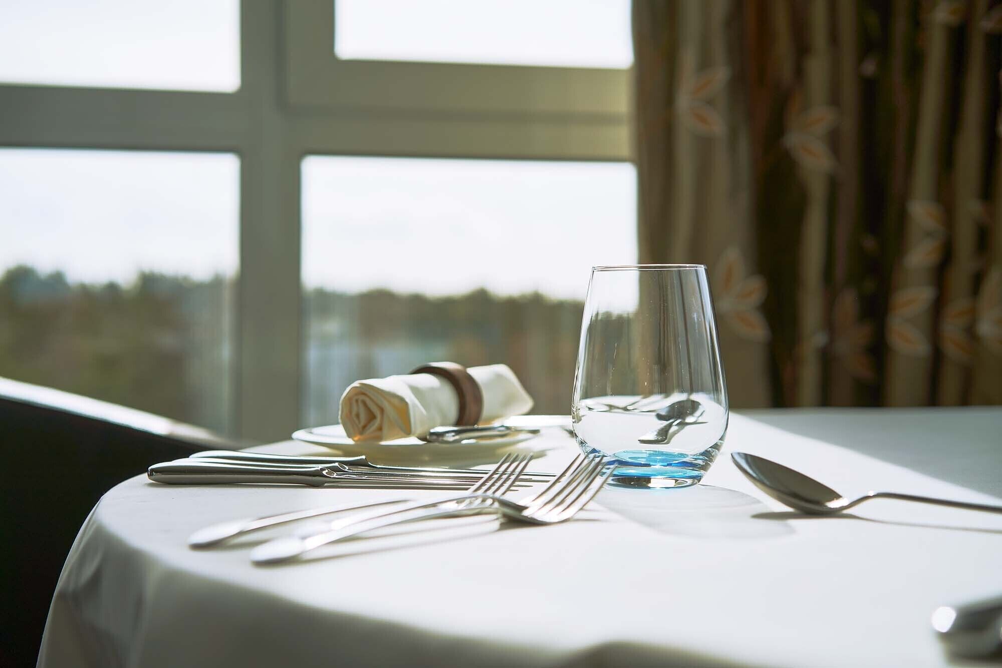 Ein gedeckter Tisch mit einem Glas Wasser, einem gefalteten Servietten und Besteck.