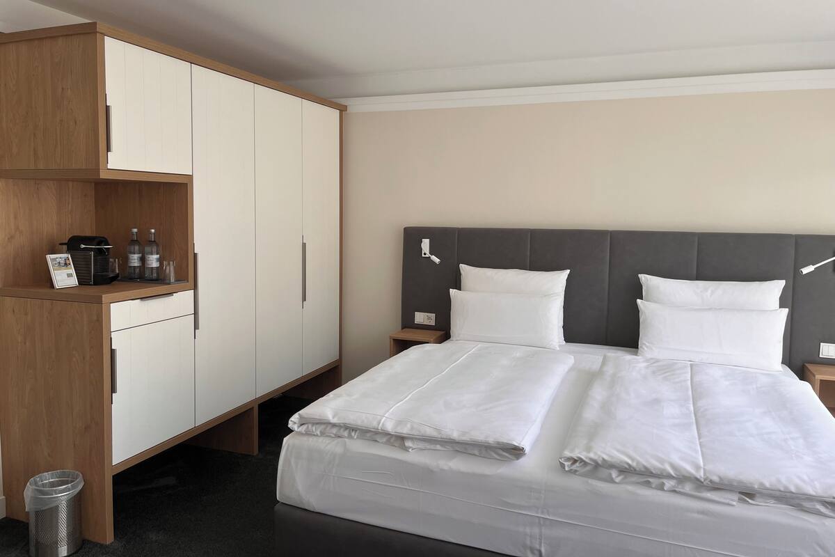 Ein Hotelzimmer mit einem Bett, einem Nachttisch, einem Holzschrank und einer Mülltonne.