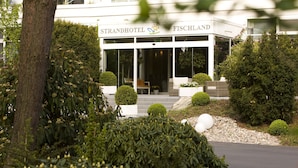 Ein modernes Hotel mit Glasfassade, Sitzgelegenheiten im Freien und gepflegter Bepflanzung.